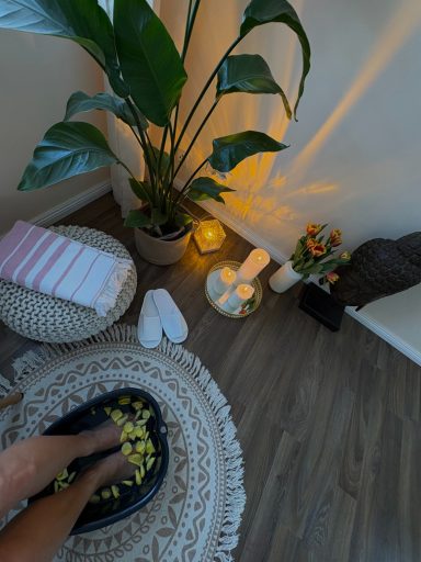 Füße in einer Fußbadewanne mit Pflanzen, Kerzen und einer gemütlichen Umgebung.