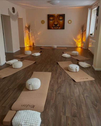 Meditaionsraum mit yogi-Matten, Kissen und einem Buddha-Gemälde an der Wand.