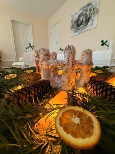 Dekorativer Tisch mit einer leuchtenden Szenerie aus Orangen, Tannenzapfen und einer Figur.