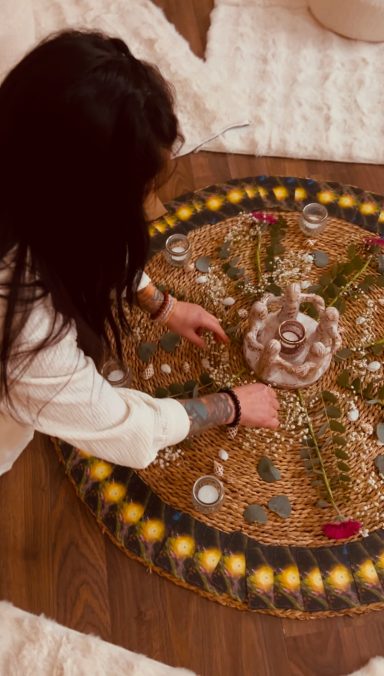 Frau gestaltet ein Mandala mit Steinen, Blumen und anderen natürlichen Materialien.