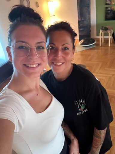 Zwei Frauen lächeln in einem hellen Raum in die Kamera.