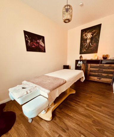 Ein entspannender Massageraum mit Tisch, sanfter Beleuchtung und dekorativen Bildern.